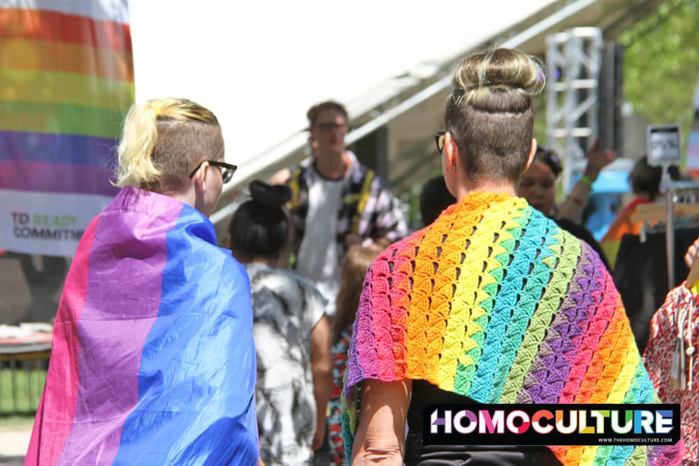 A mother and daughter dressed in Pride flags walking through a Pride festival.
