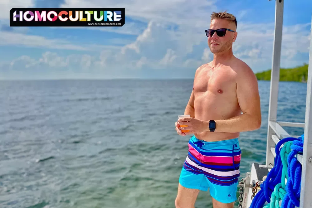 A buff gay man, holding a cocktail, on a boat, in the Florida Keys.