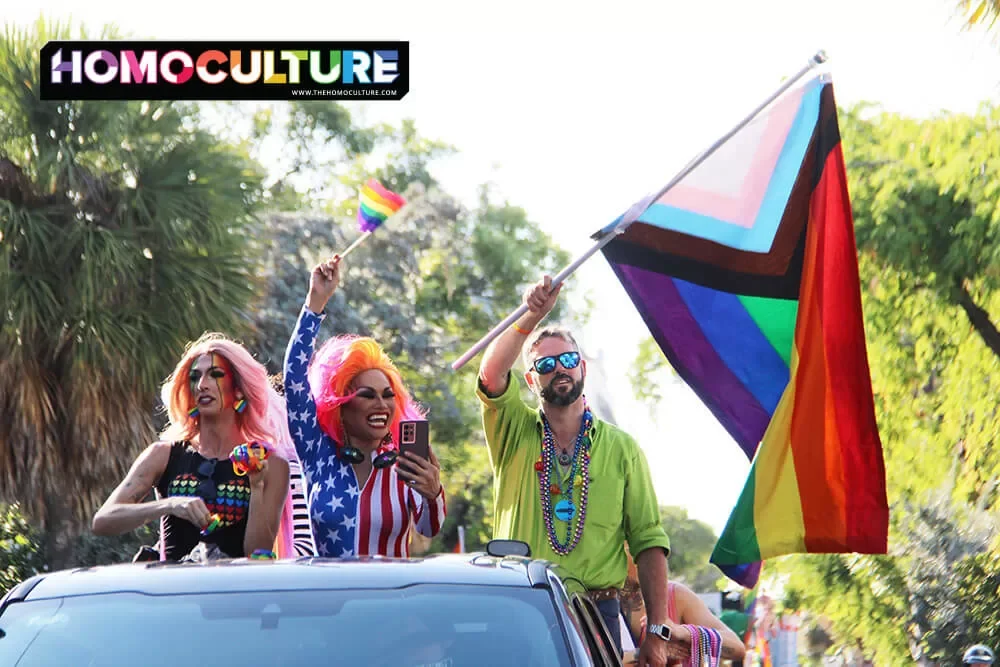 A man carries a Progressive Pride flag while riding with two drag queens in the 2023 Key West Pride parade. 