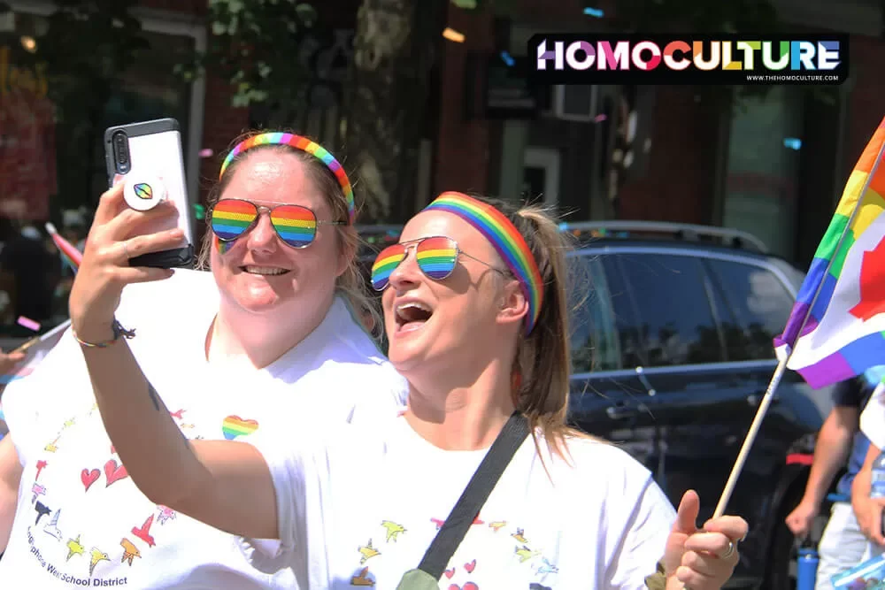 Two friends wearing Pride accessories taking a selfie in the 2023 Fredericton Pride Parade. 