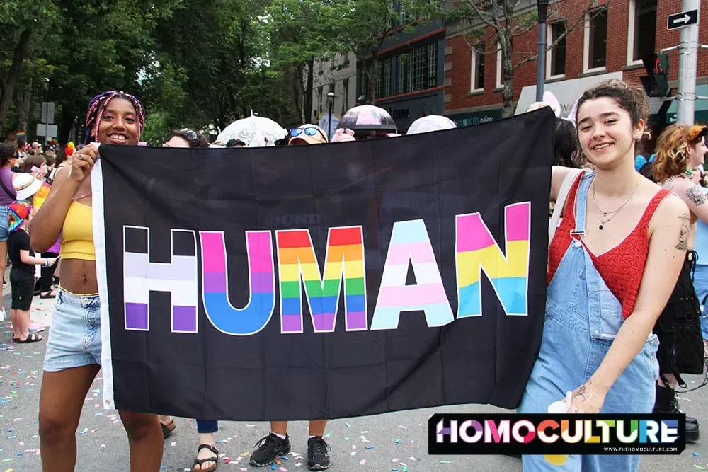 Two people holding up a HUMAN Pride flag in the 2023 Fredericton Pride Parade. 