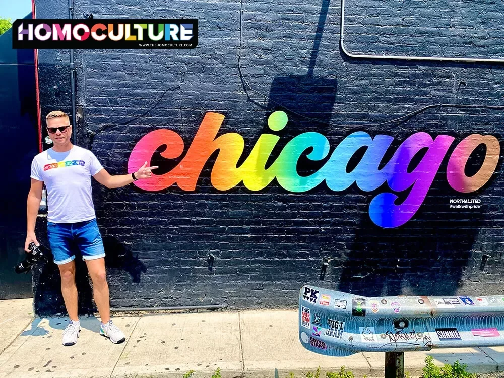 A gay man staying by a rainbow-painted Chicago sign in the Northalstad neighborhood in Chicago, Illinois.