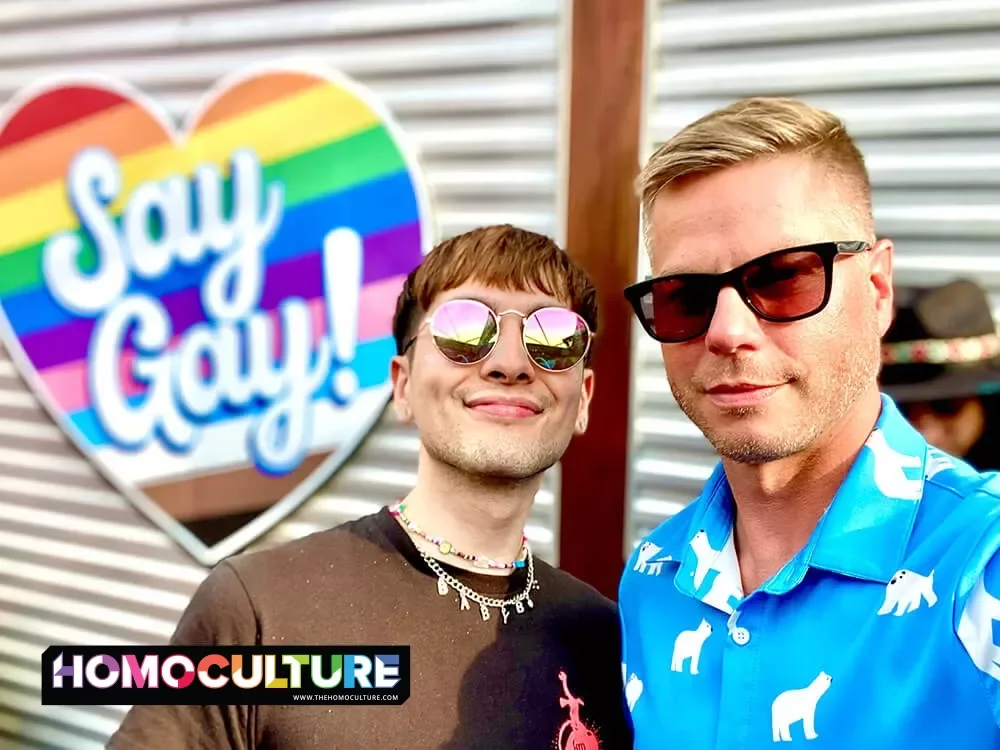 Two gay guys on the rooftop bar at Sidetracks in Chicago, Illinois with a rainbow heart in the background that says "Say Gay".