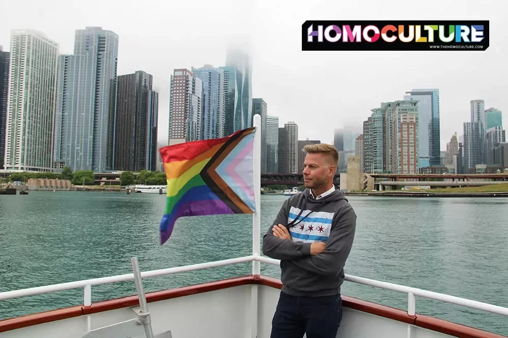 A gay guy standing near a Progressive Pride flag on the Chicago Architecture Foundation Center River Cruise.