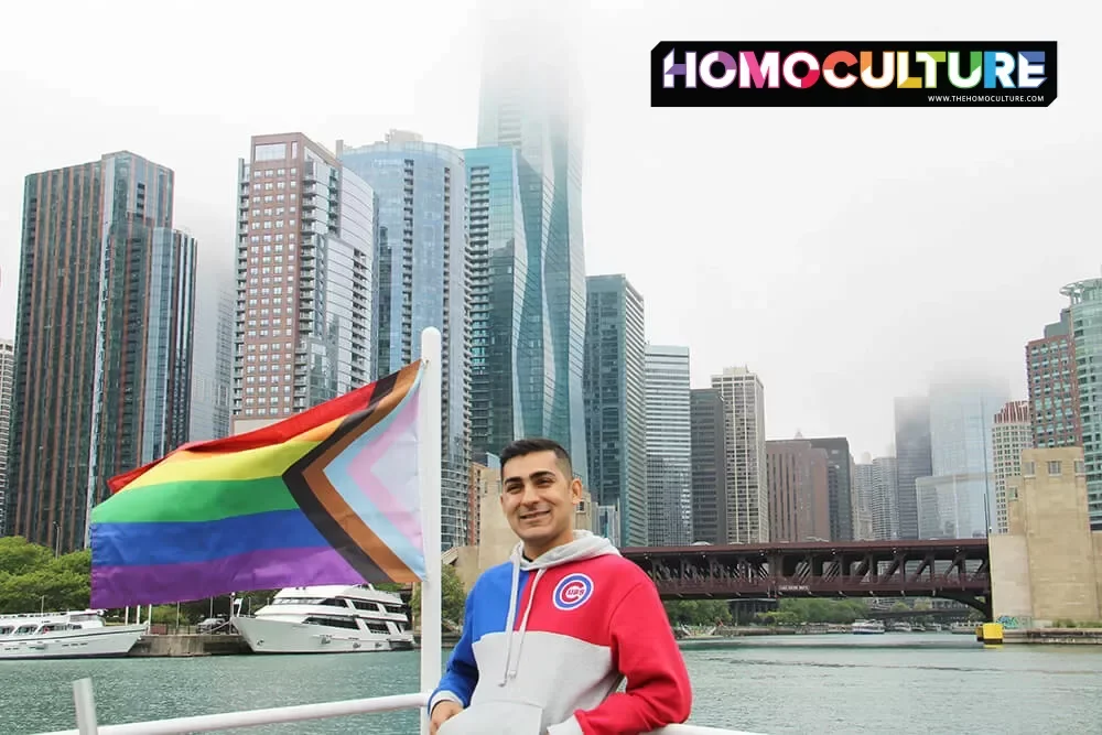 A gay guy standing near a Progressive Pride flag on the Chicago Architecture Foundation Center River Cruise.