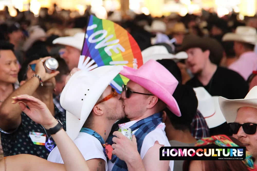 A gay couple wearing cowboy hats kiss at the 2023 Calgary Stampede 10th Annual Pride Day.