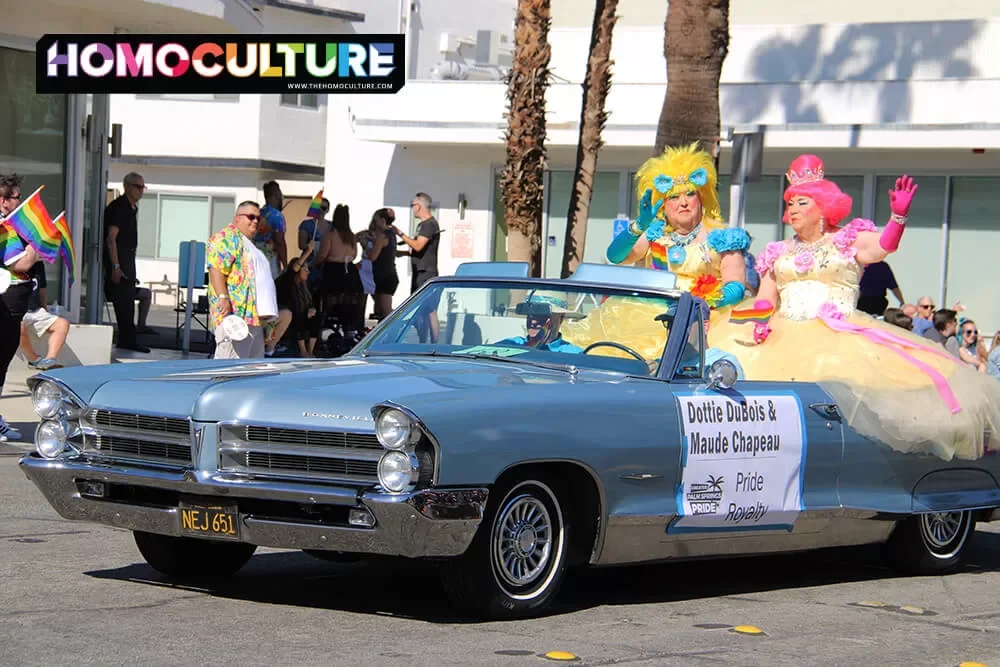 Two drag queens riding in the back of a convertible in the 2022 Palm Springs Pride parade. 