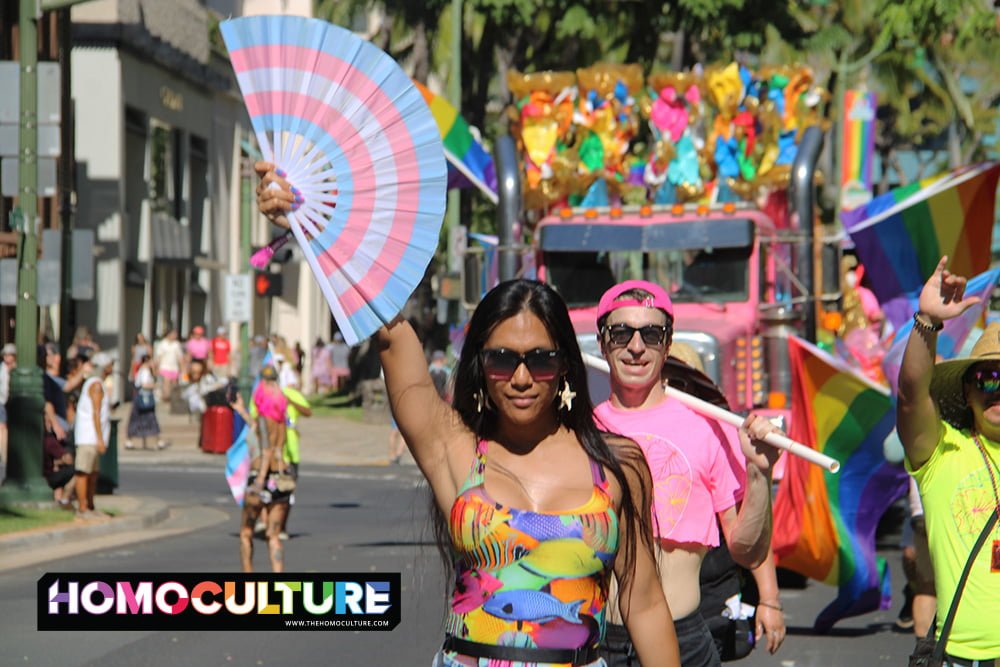 A trans person holding a trans pride fan in a Pride parade.