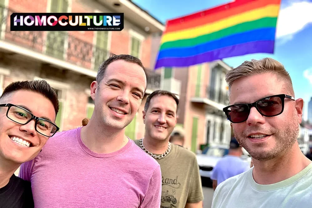 A group of friends celebrating Southern Decadence with a Pride flag in the background.