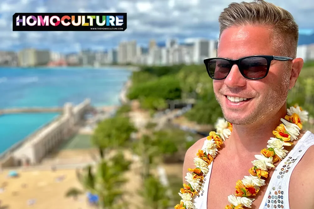 Gay man in sequin tank top, wearing sunglasses, and traditional lai, with Honolulu in the background.