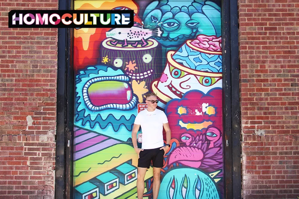 A gay man stands in front of a mural in downtown Denver, Colorado.