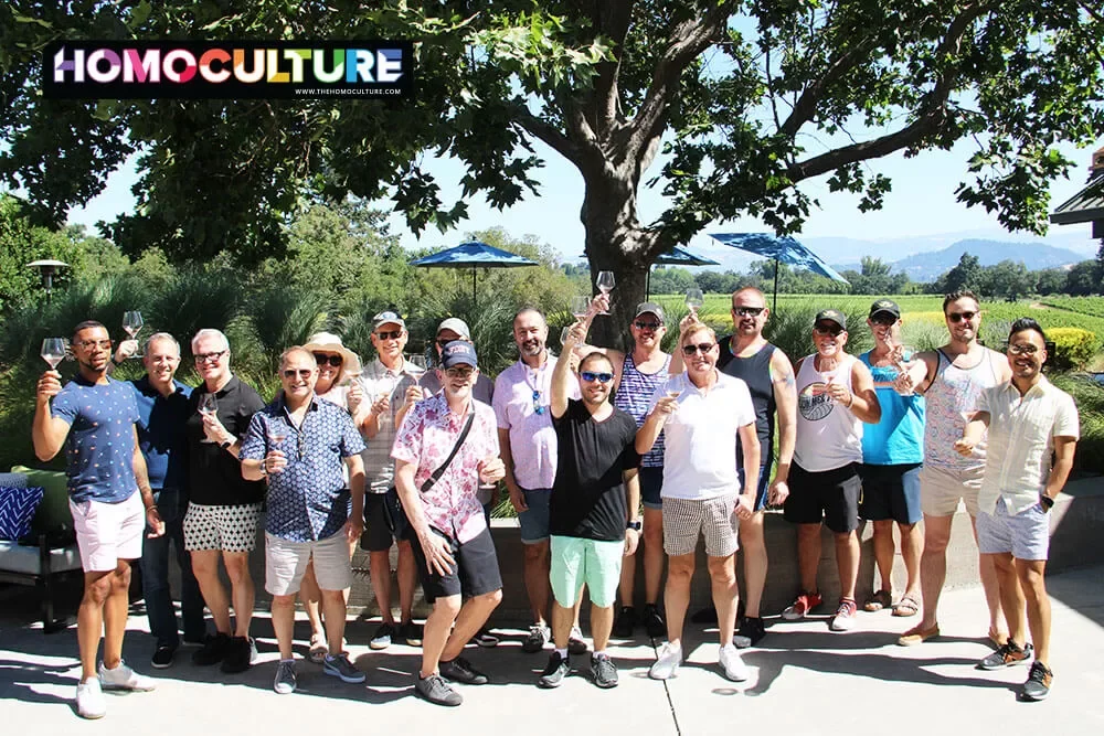 A large group raising their wine glasses during a wine tour at Gay Wine Weekend 2023. 