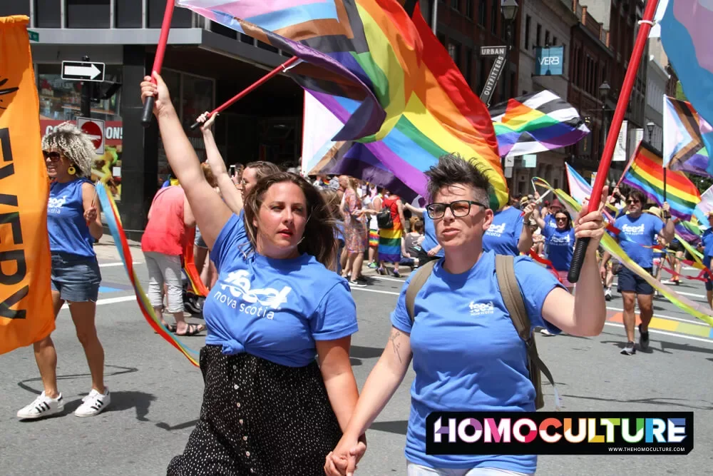 Two lesbians holding hands, carrying Pride flags, at the 2022 Halifax Pride parade. 