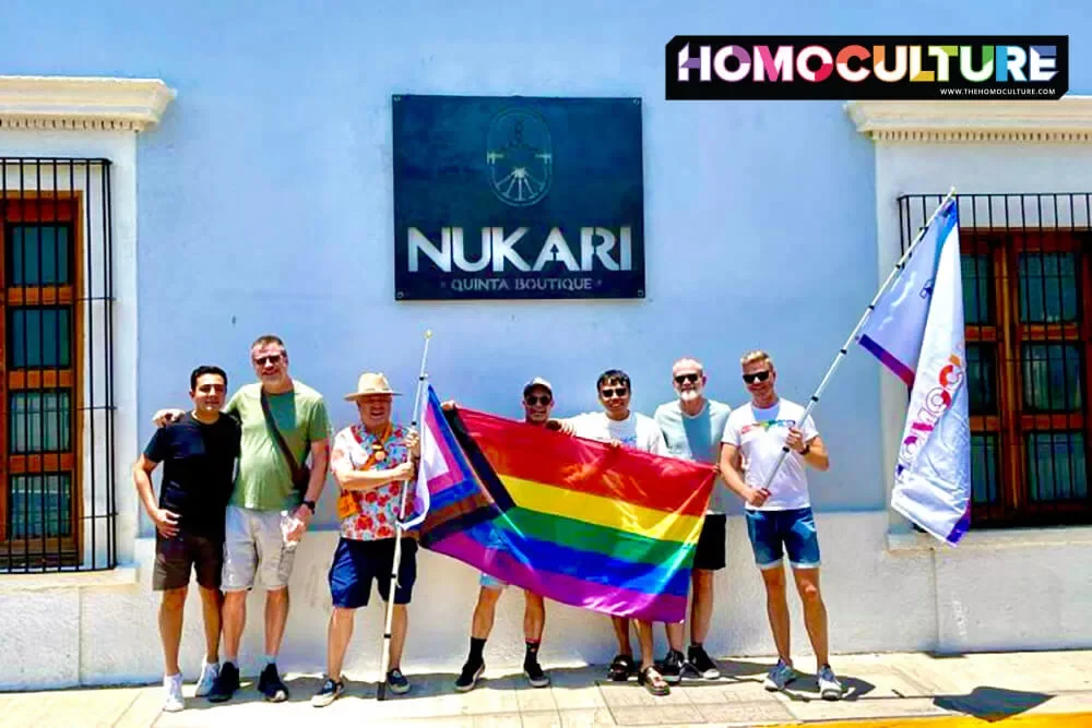 A group of gay men standing out front of the Hotel Nukari in Jala, Mexico, holding Pride flags.