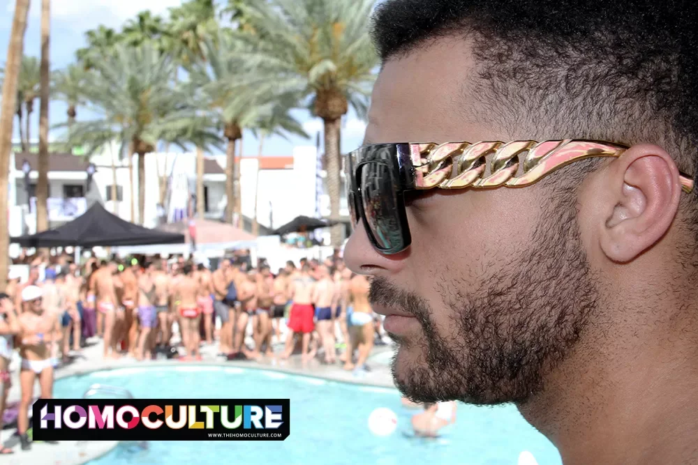A man wearing big, chunky, gold and black sunglasses at a pool party. 
