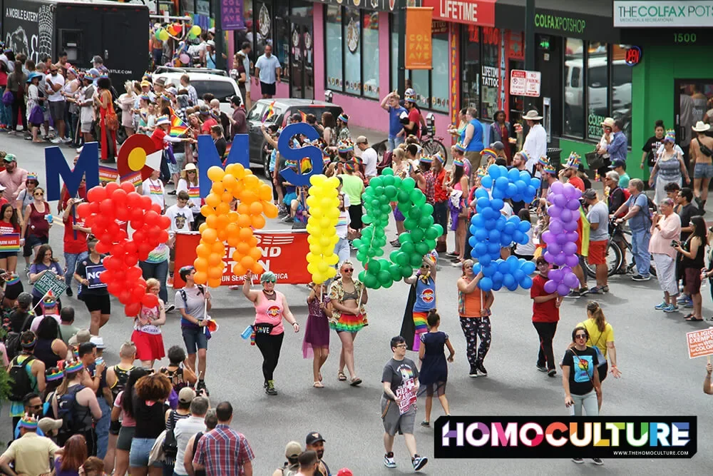People marching in a gay Pride parade holding a balloons that spell out Pride.