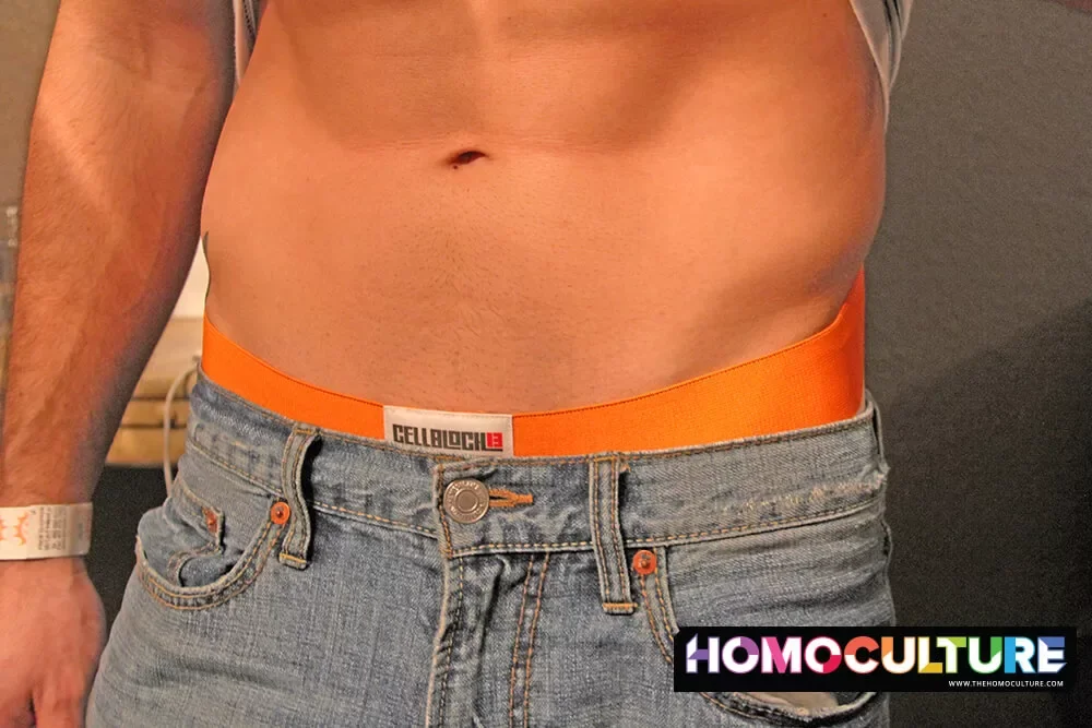 A vaccinated gay man with abs, wearing a jockstrap and jeans.