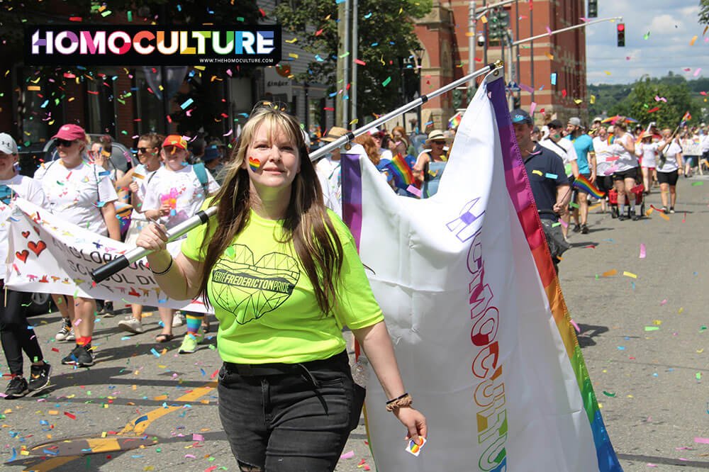A woman in a Pride parade carrying a HomoCulture flag.