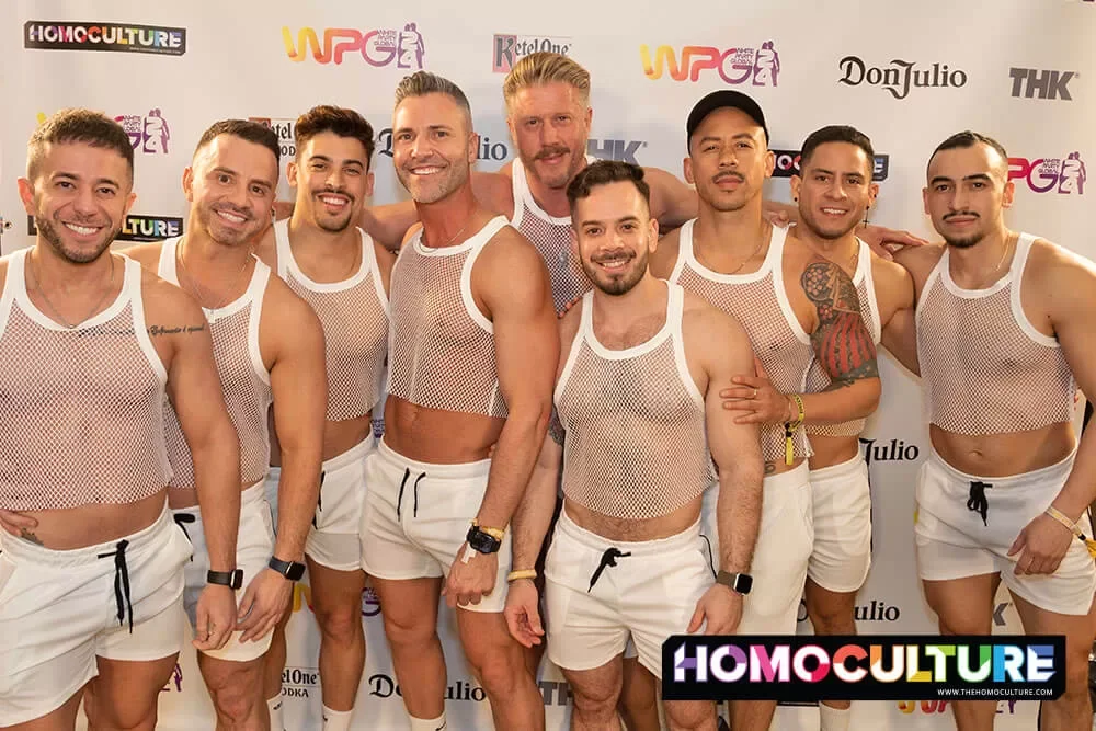 A group of friends in matching outfits stop for a photo on the white carpet at the White Party Palm Springs 2024 Saturday night White Party Sahara Desert Nights party. 