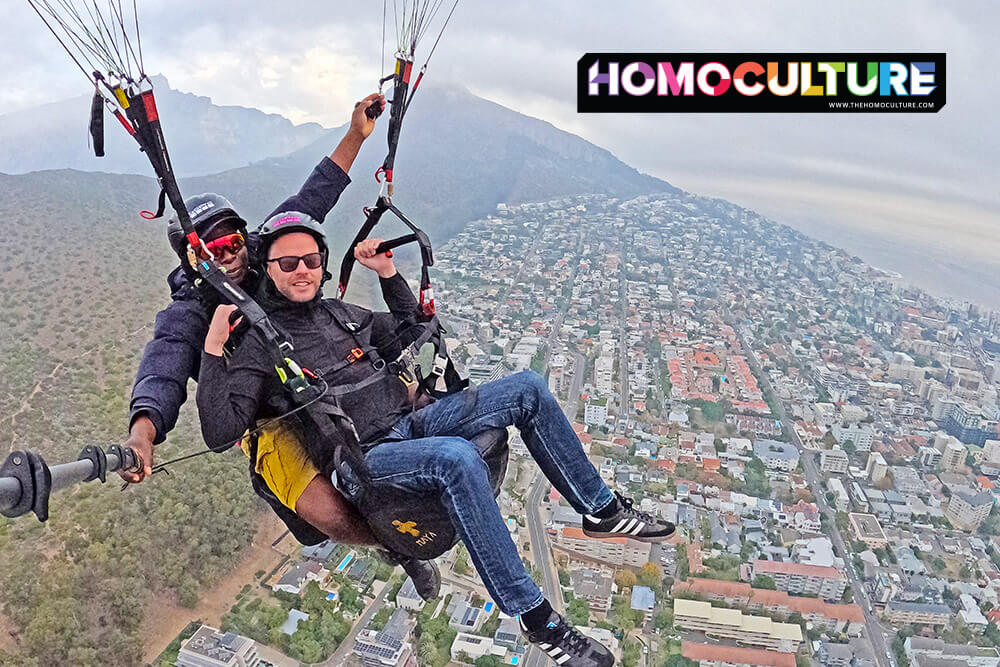 Tandem paragliders soaring above Cape Town with city streets, buildings, and mountains visible below.