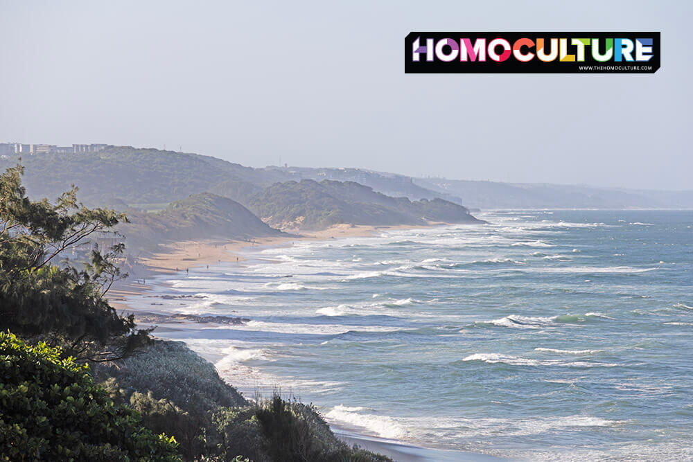 Scenic view of Durban’s coastline with waves, sandy beaches, and rolling green hills on a hazy day.