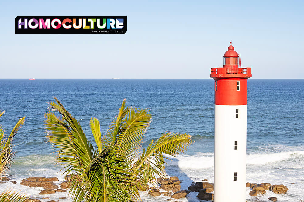 Iconic red and white Umhlanga Lighthouse overlooking the Indian Ocean, with palm trees and waves in the foreground near Durban, South Africa.