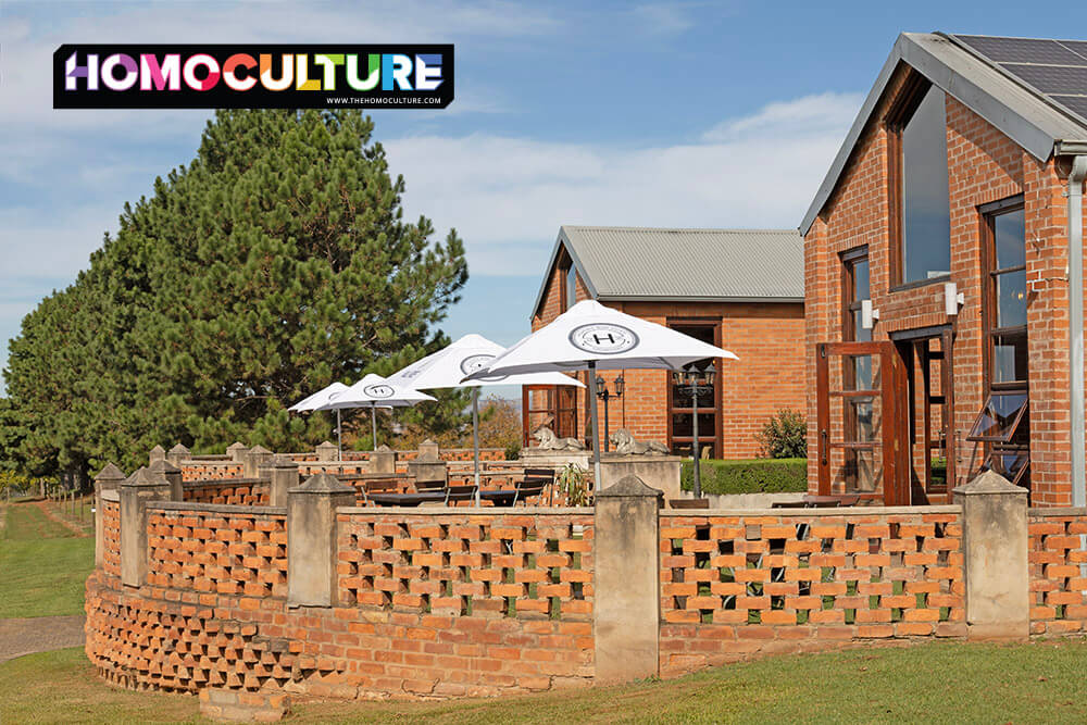 Outdoor patio and tasting terrace at Highgate Wine Estate near Durban, South Africa, featuring red brick architecture, white umbrellas, and vineyard views on a sunny day.