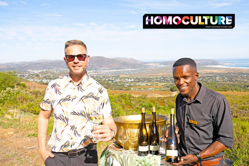 Gay traveler enjoying a private wine tasting experience with a Cape Point Vineyards staff member at the top of the vineyard, overlooking Noordhoek and the ocean, arranged through Jeep Tours Cape Town.