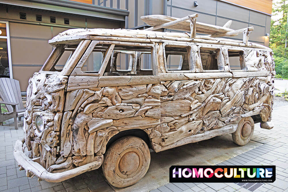 Full-size Volkswagen van sculpture made entirely of driftwood, complete with a surfboard on top, displayed in the courtyard of Hotel Zed Tofino as a playful and artistic tribute to coastal road trip culture.