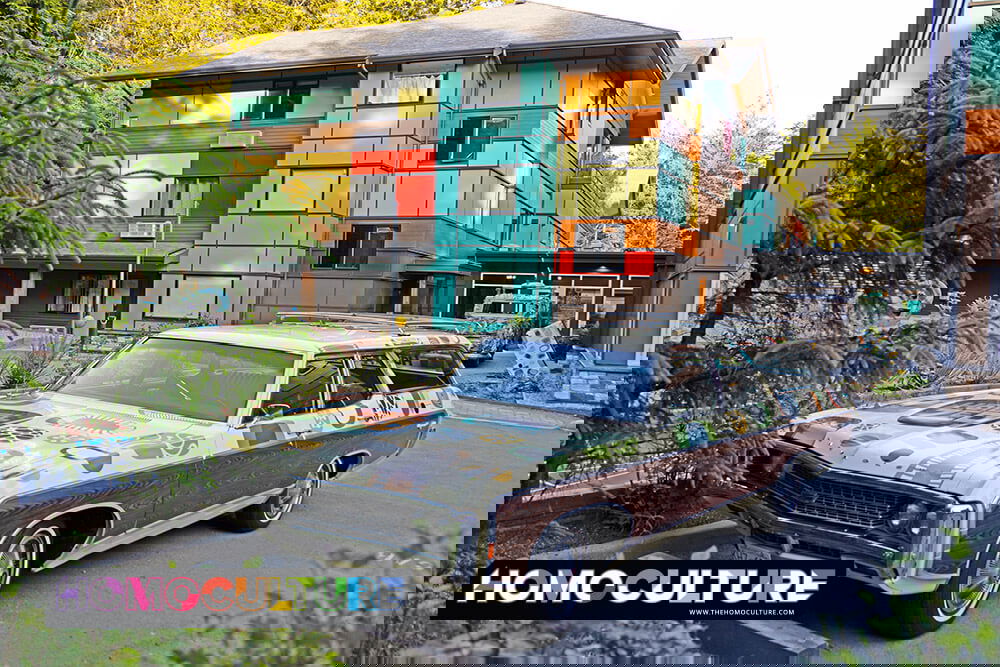 Hotel Zed Tofino exterior featuring its bold, colorful facade with a classic retro station wagon parked out front and a driftwood VW van sculpture visible in the background near the covered hotel entrance.