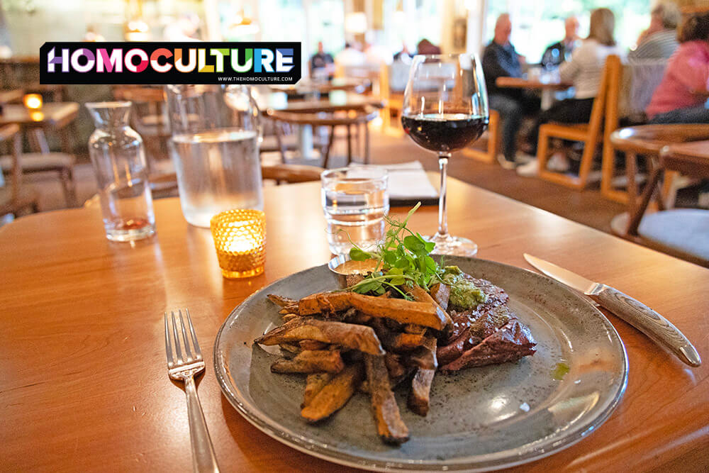 Plated steak frites with chimichurri sauce and hand-cut fries served at ROAR restaurant in Hotel Zed Tofino, paired with a glass of red wine on a wooden dining table with soft ambient lighting.