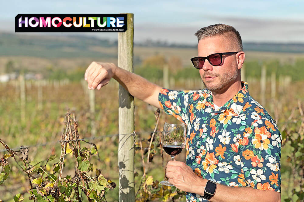 Gay man in a floral shirt holding a glass of red wine while posing in the vineyard at Highgate Wine Estate near Durban, South Africa