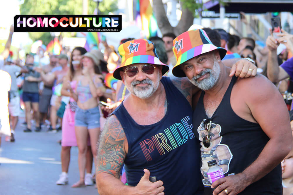 Two gay men wearing rainbow hats at a Pride parade.